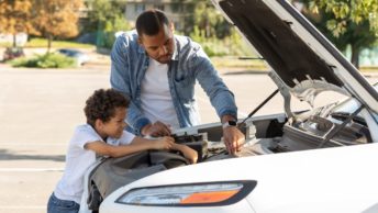 Une homme répare sa voiture lui-même et son fils le regarde